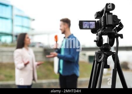 Jeune journaliste interviewant femme d'affaires dans la rue de ville, se concentrer sur l'affichage de caméra Banque D'Images