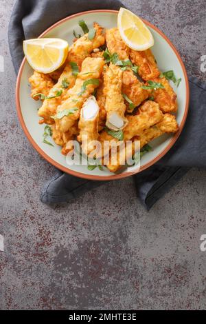 Des bandes de calmars dorées cuites et frites avec un zeste de citron sur l'assiette de la table. Vue verticale du dessus Banque D'Images