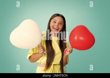 Jolie petite fille de l'adolescence jouant avec le ballon en forme de coeur rouge. Visage de fille heureux, émotions positives et souriantes. Banque D'Images