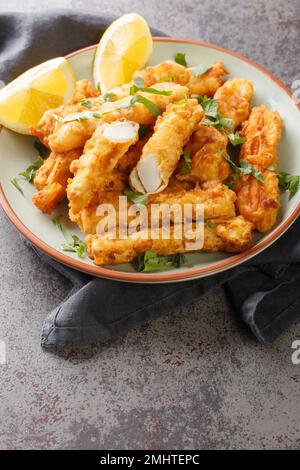 Des bandes de calmars dorées cuites et frites avec un zeste de citron sur l'assiette de la table. Verticale Banque D'Images