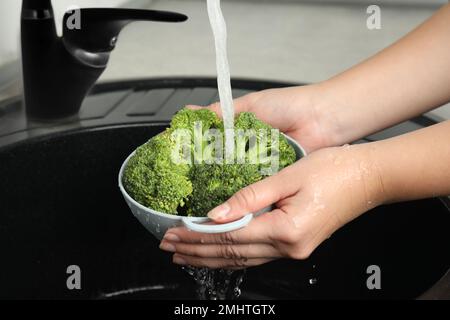 Femme lavant du brocoli vert frais dans un évier de cuisine, en gros plan Banque D'Images