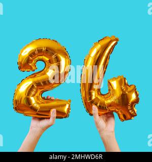 un homme caucasien tient quelques ballons en forme de nombre doré formant le numéro 24 sur un fond bleu Banque D'Images