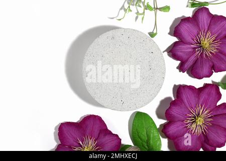 Un podium en béton avec des fleurs de clematis roses, pour la présentation de l'emballage et des cosmétiques, vue du dessus, sur fond blanc. Affichage du produit Banque D'Images