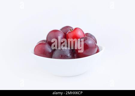 Prunes rouges bleues fraîches dans une plaque blanche sur fond blanc. Récolter des prunes ou une recette pour les prunes. Copier l'espace Banque D'Images