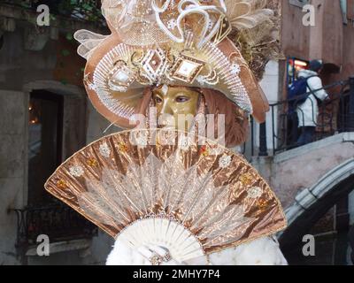 Masque sur les ponts de la lagune à Venise pendant le carnaval, dans des tons or et blanc avec ventilateur et adresse fantaisie. Venise, Italie, 10 février, 2 Banque D'Images