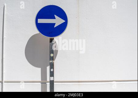 Un panneau de signalisation bleu à sens unique contre un mur blanc avec de fortes ombres en plein soleil dans une rue au Portugal Banque D'Images