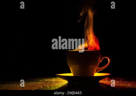 Un mug avec une boisson chaude et de la vapeur bouclés se lève, illuminé en rouge-jaune, orange sur fond noir, espace de copie, créatif, silhouette. Matin Banque D'Images