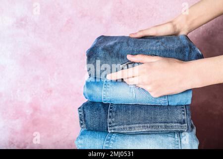 Femme pliage élégant Jean sur fond rose, gros plan Banque D'Images