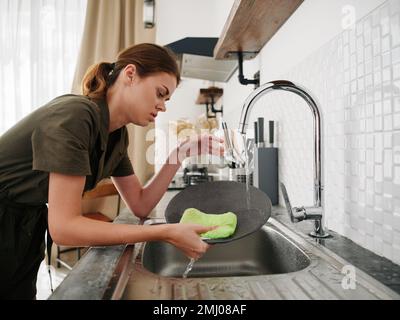 Femme fatiguée et irritée mains sans gants lave la vaisselle avec une éponge de lavage de vaisselle, des tâches ménagères, pas de lave-vaisselle, consommation d'eau élevée. Élégant Banque D'Images