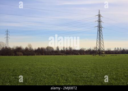 Champ cultivé avec des pylônes d'électricité et des câbles au-dessus de la tête par une journée nuageux dans la campagne italienne Banque D'Images