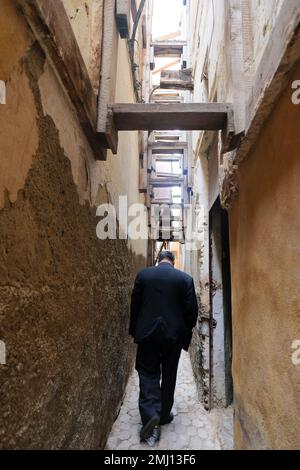 Fez, Maroc - un grand homme marche dans une ruelle étroite à Fès el Bali. Au-dessus, des planches de bois sont clouées entre les bâtiments pour les maintenir debout. Banque D'Images