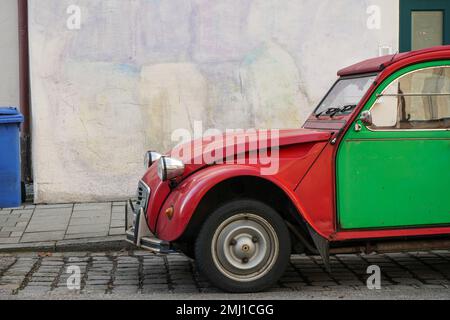 Une Citroën rouge 2CV, généralement appelée canard en Allemagne et en Autriche, avec toit ouvrant et portes vertes sur le côté de la route devant un mur de maison. Banque D'Images