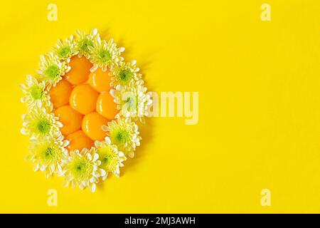 Jaunes frais crus disposés en forme d'œuf décoré de fleurs sur fond jaune. Concept de Pâques inhabituel. Aliments contenant des protéines. Banque D'Images