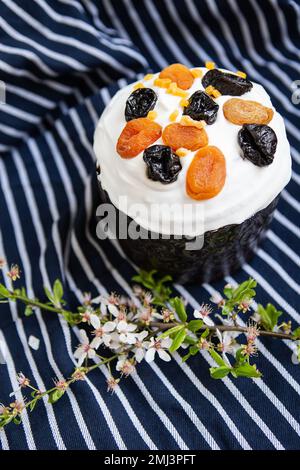 Le gâteau de Pâques, décoré d'abricots et de pruneaux séchés, se dresse sur un tablier bleu rayé, une branche fleurie. Concept de vacances religieuses de Pâques Banque D'Images