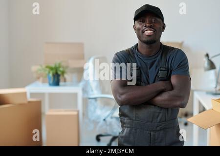 Portrait d'un chargeur afro-américain debout avec ses bras croisés au bureau et souriant à la caméra Banque D'Images