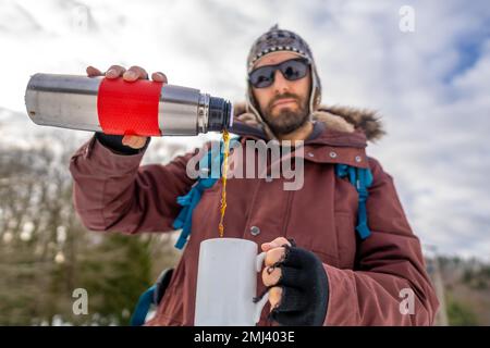Homme ayant petit déjeuner un café chaud d'un thermos en hiver dans la neige avant de commencer le trekking Banque D'Images
