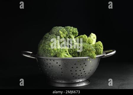 Délicieux brocoli frais en passoire sur table sur fond noir Banque D'Images