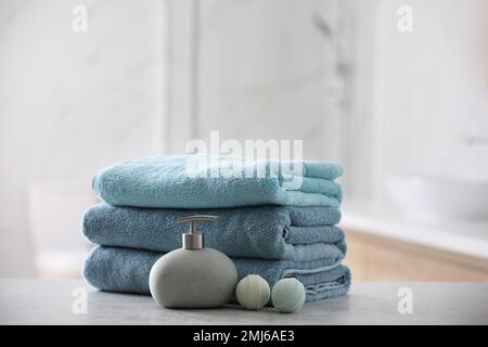 Stack of fresh towels, soap dispenser and bath bombs on table indoors Banque D'Images