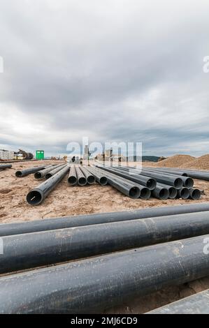 Les tubes fendus en PVC utilisés dans les puits de gaz méthane d'une décharge active sont éparpillés sur le sol, avec de l'équipement lourd dans le fond éloigné. Banque D'Images