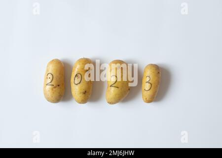 Quatre pommes de terre crues avec les chiffres 2023 écrit avec un stylo-feutre noir se trouvent sur un fond blanc, les légumes dans la nouvelle année Banque D'Images