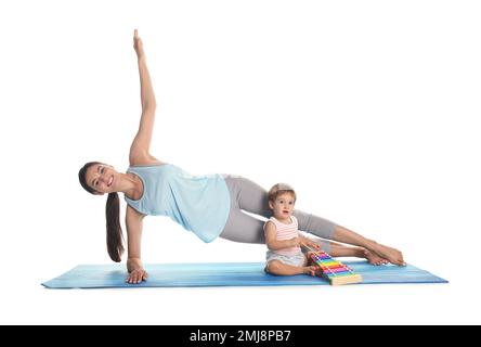 Jeune femme faisant de l'exercice pendant que son fils joue avec le xylophone jouet isolé sur blanc. Le temps de la forme physique Banque D'Images