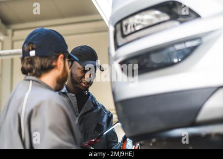 Gros plan de deux mécaniciens discutant au travail. Lumière de voiture au premier plan. Concept atelier de réparation. Photo de haute qualité Banque D'Images