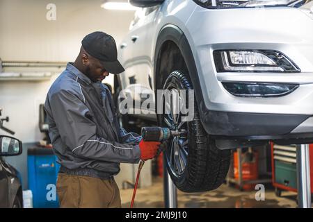 Le mécanicien qui change les pneus à l'aide d'une clé électrique est soulevé pour un processus régulier. Photo de haute qualité Banque D'Images