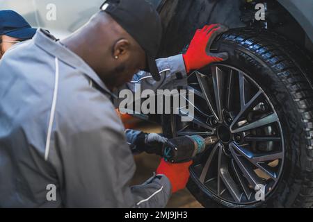 Un mécanicien remplaçant les roues d'une voiture à l'aide d'un équipement de montage de pneu à clé électrique. Photo de haute qualité Banque D'Images