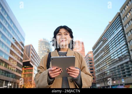 Portrait de sourires de fille coréenne heureux, marche en ville avec tablette numérique et sac à dos, utilise son gadget pour se déplacer Banque D'Images