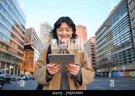 Portrait de sourires de fille coréenne heureux, marche en ville avec tablette numérique et sac à dos, utilise son gadget pour se déplacer Banque D'Images