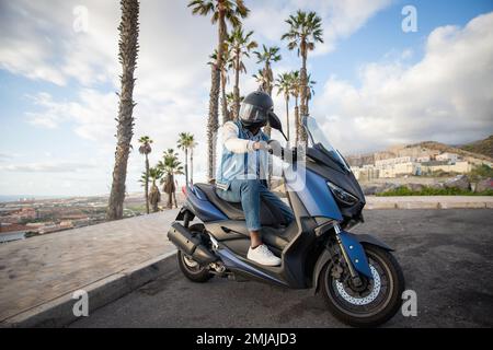 Un motard afro-américain assis sur sa moto dans un endroit tropical avec des palmiers Banque D'Images