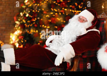 Le Père Noël repose dans un fauteuil près d'un arbre de Noël décoré à l'intérieur Banque D'Images