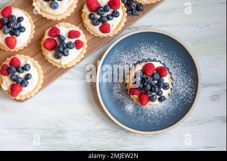 Vue de dessus des tartes à la crème vanille faites maison, recouvertes de framboises et de myrtilles. Banque D'Images