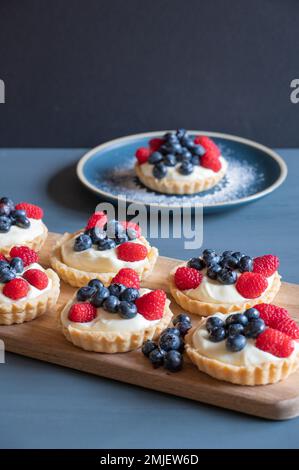 Des tartes sont placées sur une planche à découper sur une table bleue, sur un fond sombre avec un espace de copie. Banque D'Images