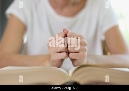 Femme s'assoit à la table avec un livre épais ouvert et tient ses poings sur les pages de livre. Banque D'Images