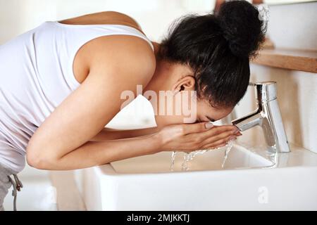 Réveillez-vous avec une touche rafraîchissante. une jeune femme se lavant le visage dans la salle de bains. Banque D'Images