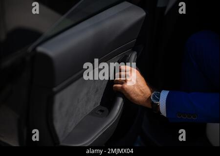 Un homme en costume bleu ouvre la porte de la voiture. Gros plan de la main d'un homme avec une montre chère. Banque D'Images