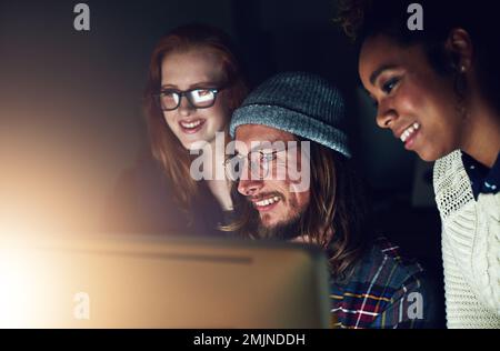 Nous avons toujours du plaisir à travailler tard. une équipe d'affaires regardant un écran d'ordinateur ensemble pendant un quart de nuit au travail. Banque D'Images