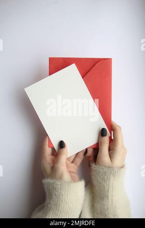 les mains des femmes dans un chandail avec manucure tenant une feuille blanche et une enveloppe rouge sur un fond blanc. mise en page carte postale Banque D'Images