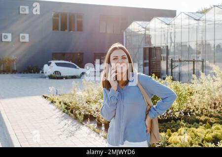 Une jeune jolie fille, vêtue d'une chemise et d'un Jean, se tient près du centre de la fleur et parle au téléphone. La femme va acheter des plantes vertes pour de Banque D'Images