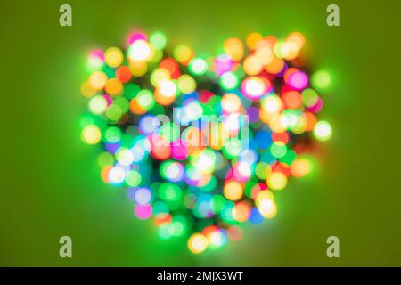 Forme de coeur composée de cercles multicolores de lumières sur fond vert vif. Fond plat pour la Saint-Valentin Banque D'Images