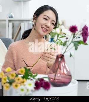 La jeune femme à la maison organisant des fleurs Banque D'Images