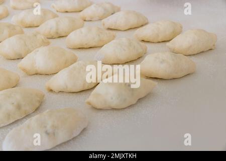 Faire des petits pains faits maison à partir de pâte de levure sur un comptoir blanc, en utilisant des pommes de terre comme garniture Banque D'Images