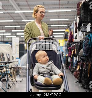 Casualy mère habillée choisissant des chaussures et des vêtements sportifs dans le rayon des sports du magasin de supermarché avec son bébé garçon enfant dans poussette Banque D'Images