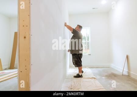 Comme les travaux en cours sur la rénovation de la maison dans le travailleur de chambre utilise la truelle de sable pour poncer la boue de mur sec Banque D'Images