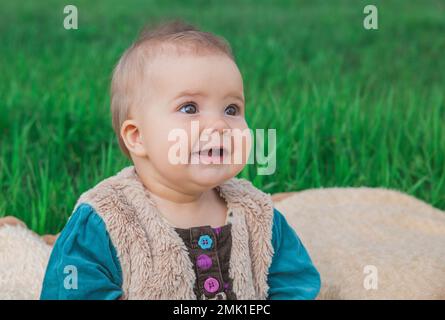 bébé sans dents dans une robe multicolore assis sur un couvre-lit sur la pelouse Banque D'Images
