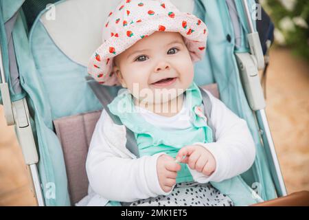 bébé en chapeau sourit sans dents assis dans une poussette bleue Banque D'Images