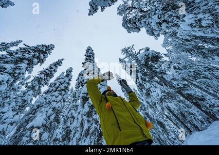 Vue à angle bas d'un jeune garçon mignon avec des bras levés et regardant dans la forêt enneigée, ISO Syote, Ostrobothnia du Nord, Laponie, Finlande Banque D'Images