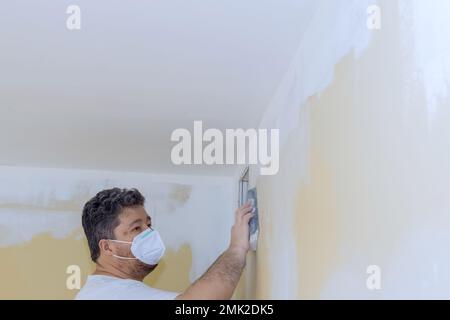 Le travailleur a poncé la boue de cloisons sèches à l'aide d'une truelle de sable au moment de la rénovation de la maison dans la pièce Banque D'Images