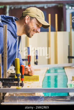 carpenter admire une table en chêne avec de la résine époxy turquoise Banque D'Images